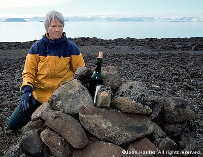 Phyllis, from aluminum sailboat Morgan's Cloud, puts a wine bottle with a message into a cairn at Skjoldungen, East Greenland