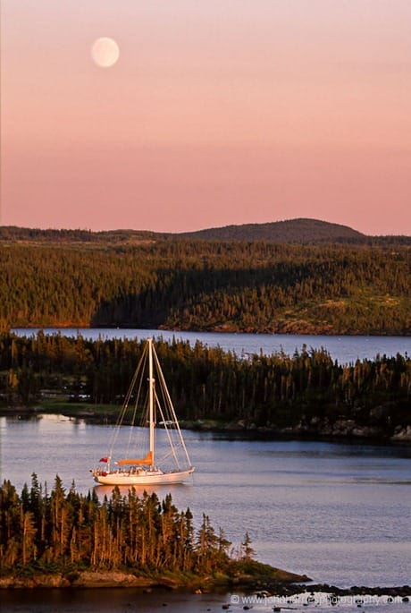 "Morgan's Cloud" lies at anchor in the glow of the setting sun and the rising moon in a sheltered tree-surrounded anchorage in Newfoundland. "Morgan's Cloud" lies at anchor in the glow of the setting sun and the rising moon at Maidens Arm, a very sheltered and uninhabited anchorage on the Great Northern Peninsula. Though uninhabited by people, we had lots of company from otters, moose and birds.